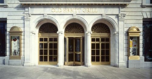 Entrance of Old Ebbitt Grill featuring arched windows and golden doors, set in a classic stone facade.