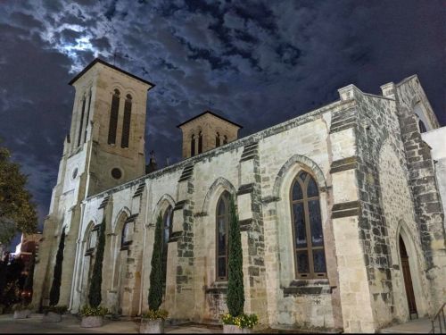 Historic stone church illuminated by moonlight under a dramatic, cloudy night sky.