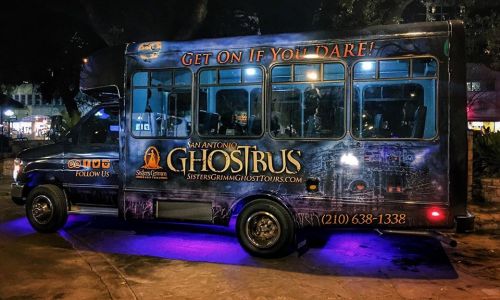 A spooky-themed bus with "San Antonio GhostBus" signage, parked at night with purple lighting.