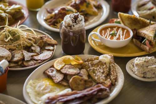 A spread of various breakfast dishes, including eggs, bacon, pancakes, and a drink in a jar, on a table.