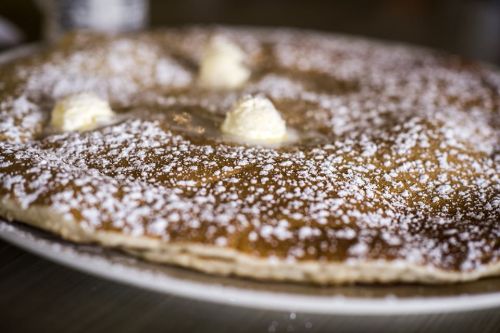 A large, fluffy pancake topped with butter and dusted with powdered sugar on a white plate.