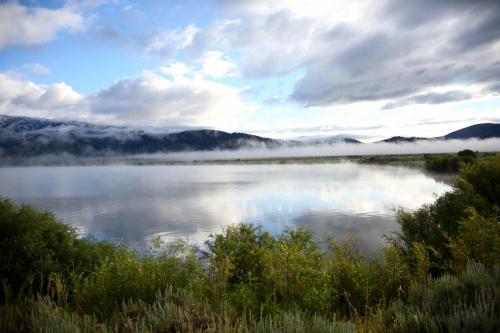 A serene lake surrounded by misty mountains and lush greenery under a cloudy sky.