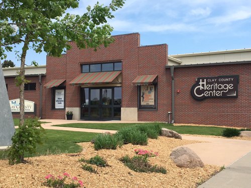 Exterior of the Clay County Heritage Center, featuring a brick facade, green landscaping, and a clear blue sky.
