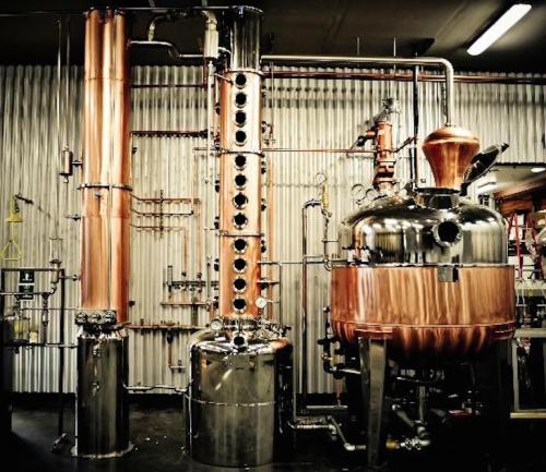 A copper and stainless steel distillation apparatus in a factory setting, featuring pipes and a large boiler.