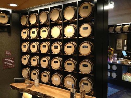 A wall display of wooden barrels arranged on shelves, with a bar area visible in the background.