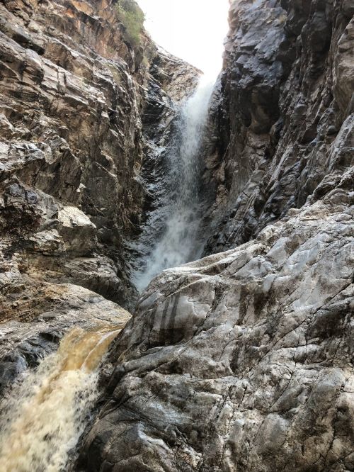 A waterfall cascading down rugged, rocky cliffs, surrounded by steep terrain and natural textures.