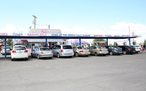 A row of parked cars outside an ice cream shop with a colorful sign advertising various treats.