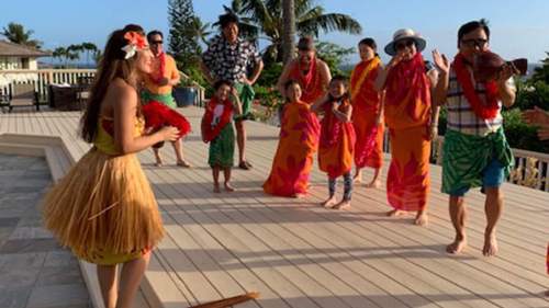A group of people in colorful attire enjoying a traditional Hawaiian dance performance outdoors.