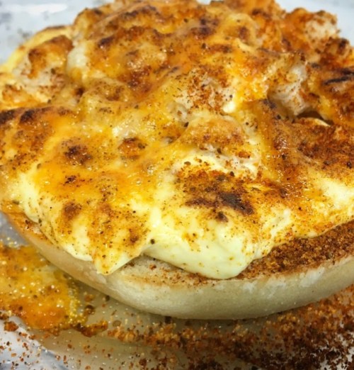 A close-up of a cheesy, baked dish with a golden crust and sprinkled seasoning on a toasted bread base.