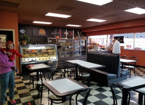A cozy café interior with black and white checkered floors, tables, a display case, and a person holding a child.