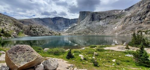 A serene mountain lake surrounded by rocky cliffs and lush greenery under a cloudy sky.