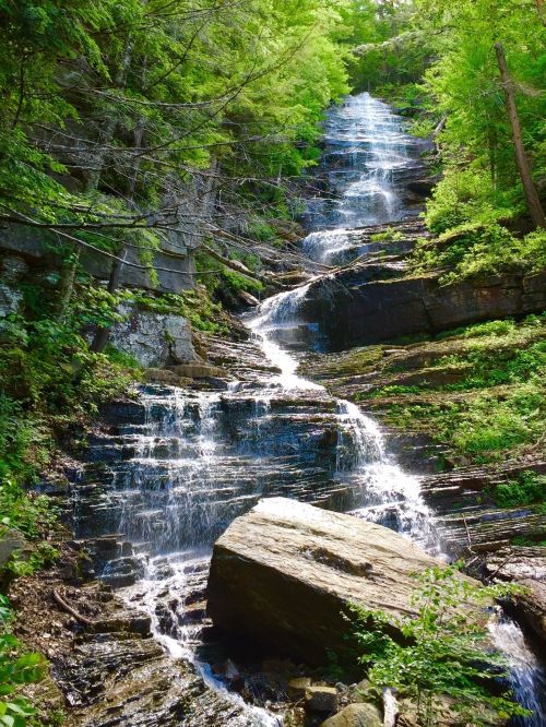 A cascading waterfall flows down a rocky cliff, surrounded by lush green trees and foliage.