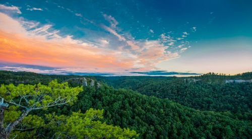 A panoramic view of lush green hills under a colorful sunset sky with scattered clouds.