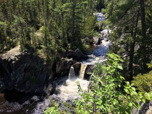 A scenic view of a waterfall cascading through rocky terrain, surrounded by lush green trees and flowing water.
