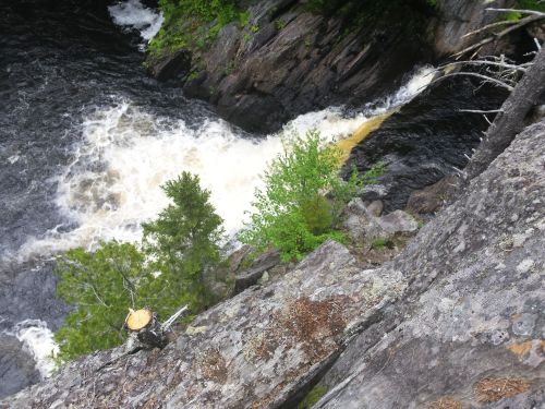 Aerial view of a rushing river flowing between rocky cliffs, surrounded by lush green trees.