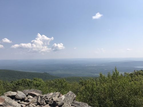 A panoramic view of rolling green hills under a clear blue sky with a few clouds. Rocks in the foreground.