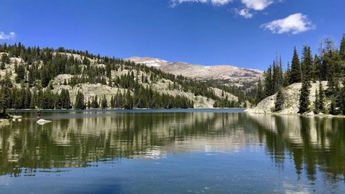 A serene lake surrounded by mountains and lush green trees under a clear blue sky.