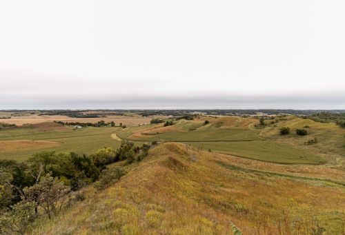 A panoramic view of rolling hills and fields under a cloudy sky, showcasing the natural landscape of the countryside.