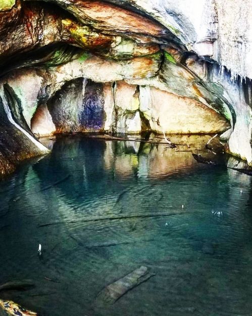 A serene cave with a clear, still pool of water reflecting colorful rock formations.