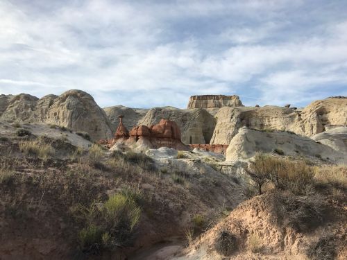 A rugged landscape featuring colorful rock formations and hills under a cloudy sky.