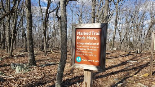 Sign at the top of Purgatory Mountain, marking the end of the trail, surrounded by bare trees and fallen leaves.