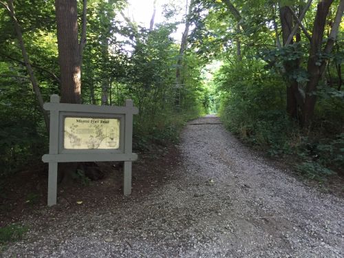 A gravel path through a lush green forest, with a sign for "Miguel's Trail" on the left.