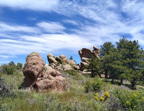 Rock formations surrounded by greenery under a blue sky with scattered clouds.