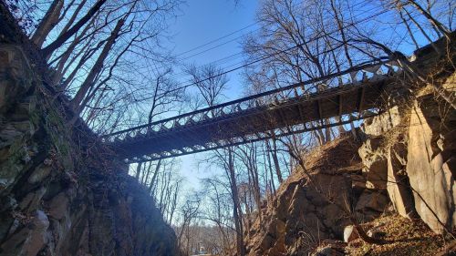 A wooden bridge spans a rocky gorge, surrounded by bare trees under a clear blue sky.