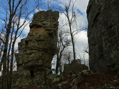 A rocky outcrop towers among bare trees under a cloudy sky, showcasing rugged natural formations.