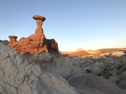 A unique rock formation with a flat top stands tall against a clear sky, surrounded by layered, colorful terrain.