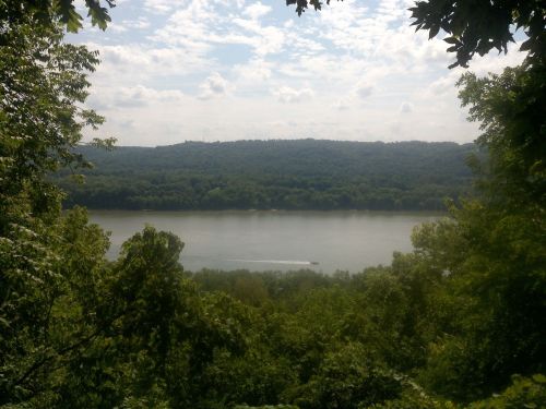 A serene river view surrounded by lush green trees under a partly cloudy sky.
