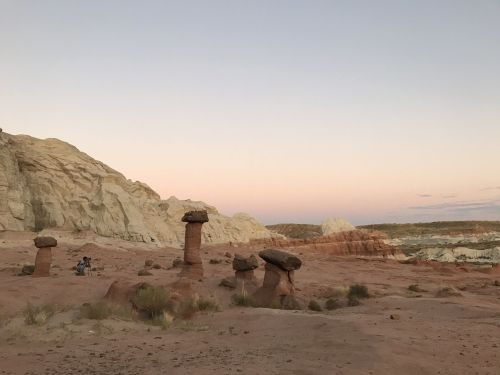 A desert landscape featuring unique rock formations at sunset, with soft pastel colors in the sky.