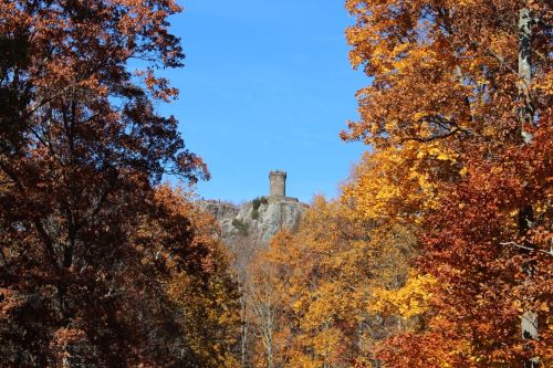 A stone tower atop a rocky hill, surrounded by vibrant autumn foliage in shades of orange and yellow.