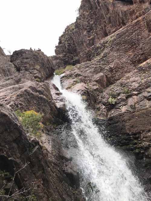 A waterfall cascading down rocky cliffs, surrounded by rugged terrain and sparse vegetation.