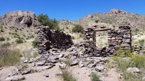 Ruins of a stone structure amidst rocky terrain and sparse vegetation under a clear blue sky.