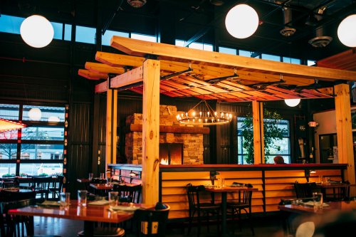 Cozy restaurant interior featuring wooden beams, a stone fireplace, and round pendant lights.