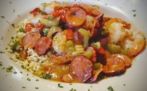 A colorful dish featuring shrimp, sausage, and vegetables served over rice, garnished with herbs.
