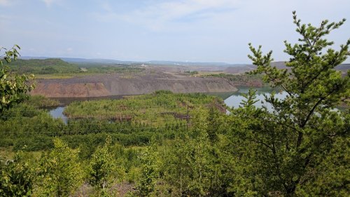 A scenic view of a landscape with a lake, green trees, and rocky hills under a clear sky.