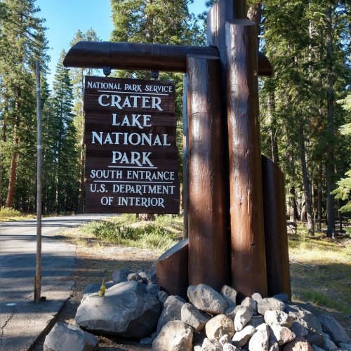Sign for Crater Lake National Park's south entrance, surrounded by trees and rocks.
