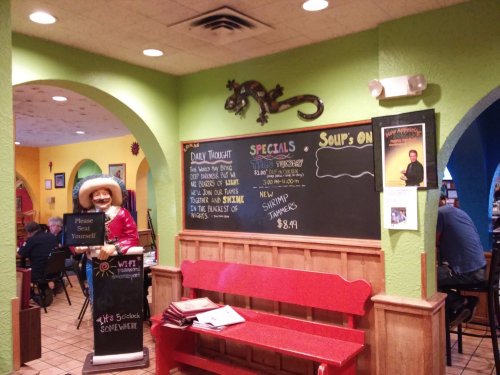 Colorful restaurant interior featuring a cowboy statue, chalkboard specials, and a vibrant green wall.
