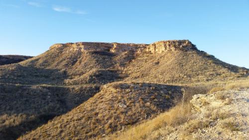 A rugged hillside with dry grass and rocky outcrops under a clear blue sky.