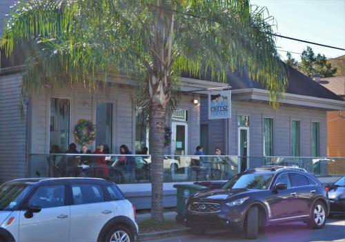 A cozy restaurant with outdoor seating, surrounded by palm trees and parked cars on a sunny day.