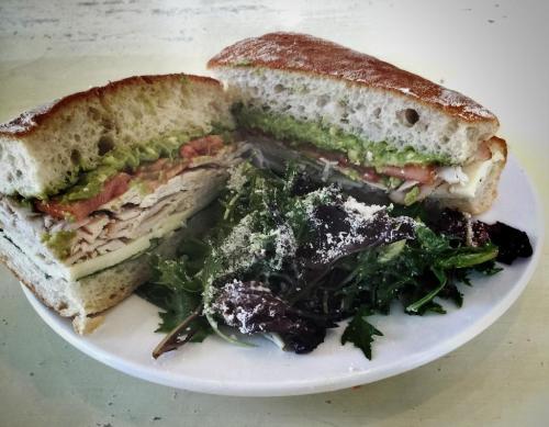 A sandwich filled with turkey, lettuce, tomato, and avocado, served with a side of mixed greens on a white plate.