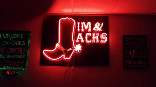 Neon sign for "Jim & Jack's" featuring a cowboy boot, with a chalkboard menu on the left.