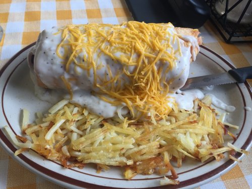 A plate featuring a large smothered burrito topped with cheese and served with crispy hash browns on the side.