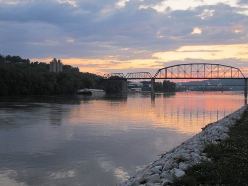 A tranquil river scene at sunset, featuring a bridge and reflections on the water, with clouds in the sky.