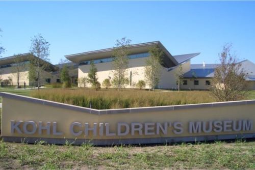 Sign for Kohl Children's Museum in front of modern buildings and landscaped greenery under a clear blue sky.