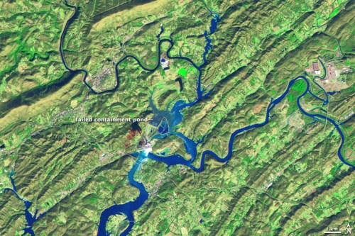 Aerial view of a landscape with a failed containment pond, rivers, and surrounding green hills.