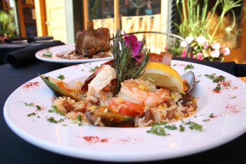 A vibrant seafood dish with shrimp, mussels, and rice, garnished with lemon, herbs, and a flower on a black table.