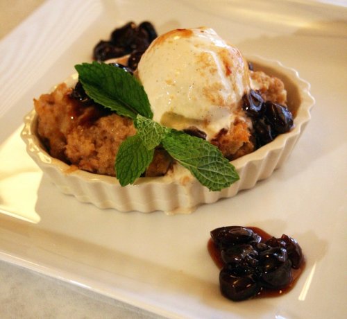 A dessert in a white dish featuring a scoop of ice cream, topped with cherries and mint leaves.